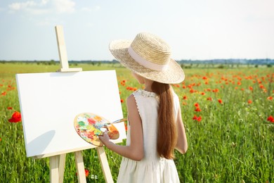 Photo of Little girl painting on easel in beautiful poppy field