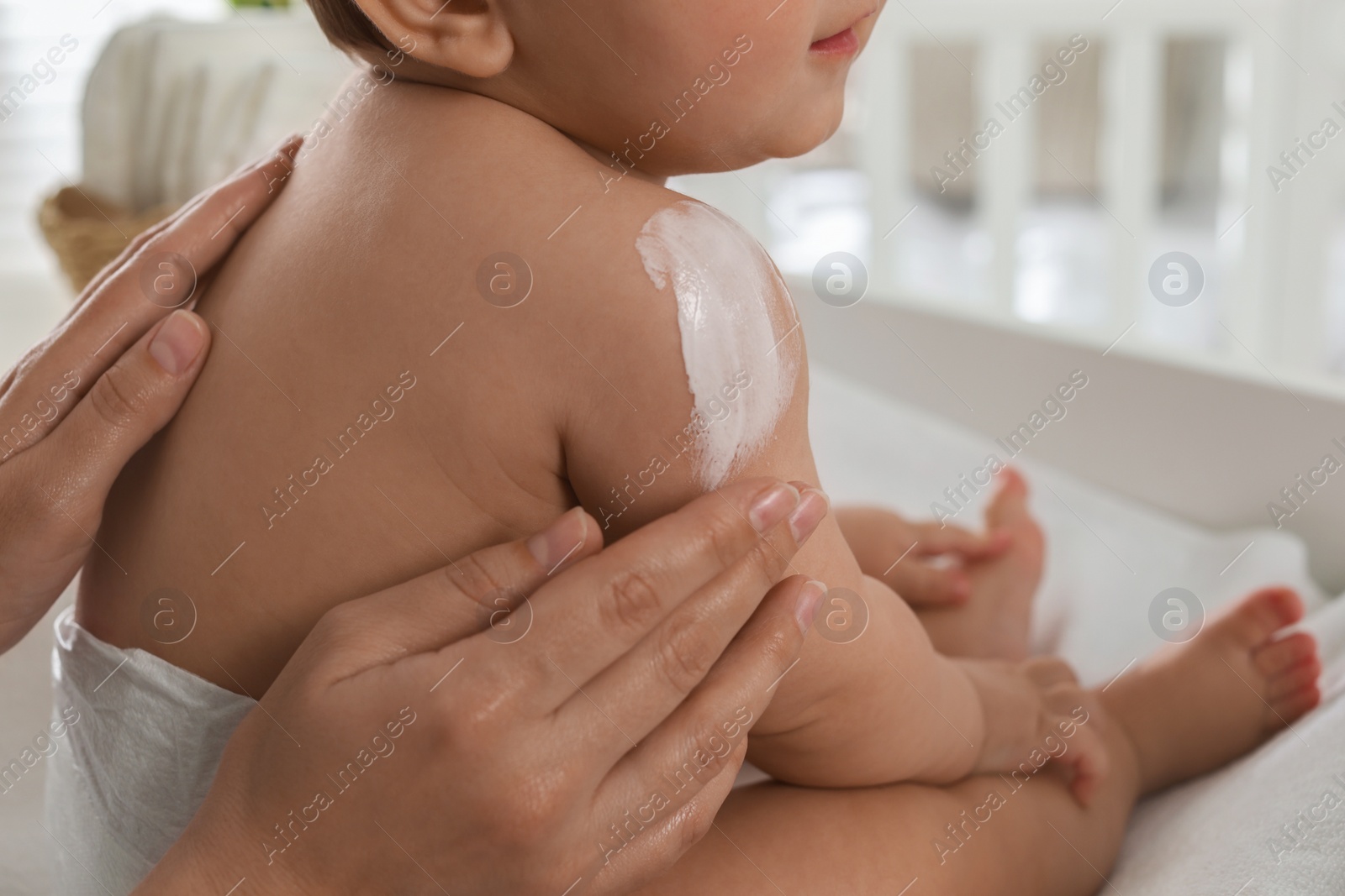 Photo of Mother applying body cream on her little baby at home, closeup