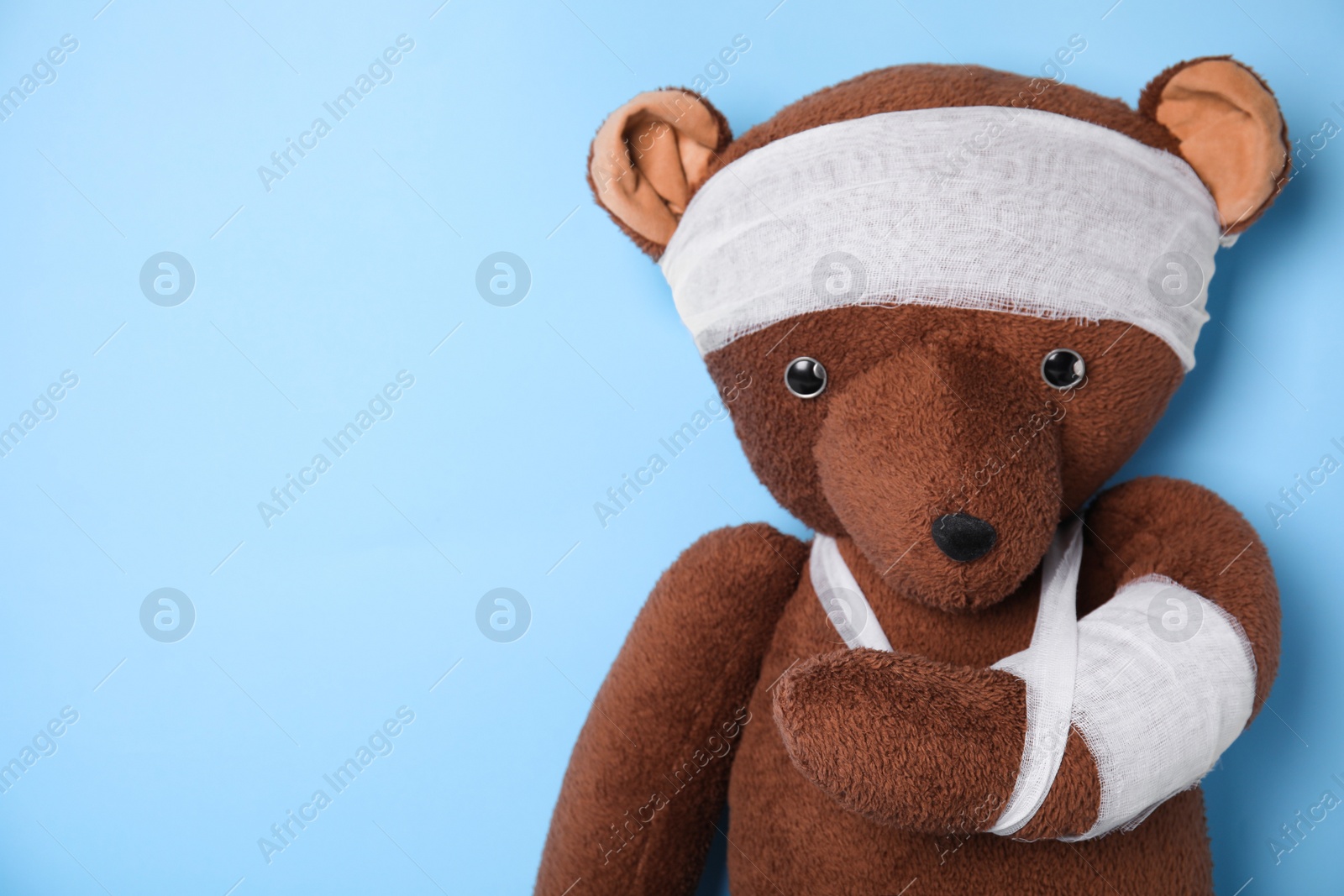 Photo of Toy bear with bandages on light blue background. Space for text