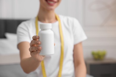 Woman holding bottle of pills in room, closeup. Weight loss