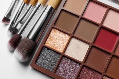 Photo of Beautiful eye shadow palette and brushes on white table, flat lay