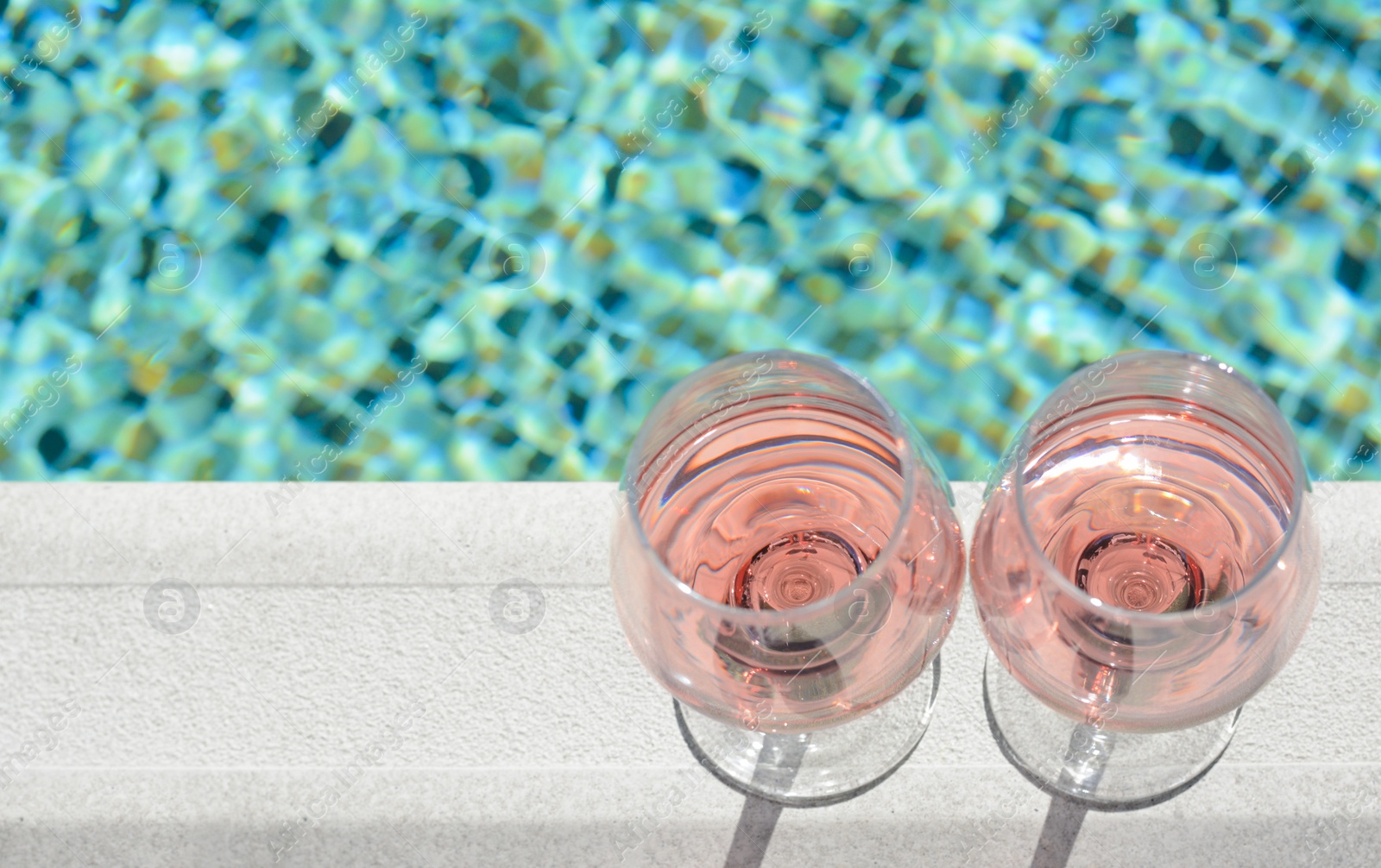 Photo of Glasses of tasty rose wine on swimming pool edge, above view. Space for text