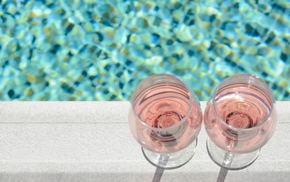 Glasses of tasty rose wine on swimming pool edge, above view. Space for text