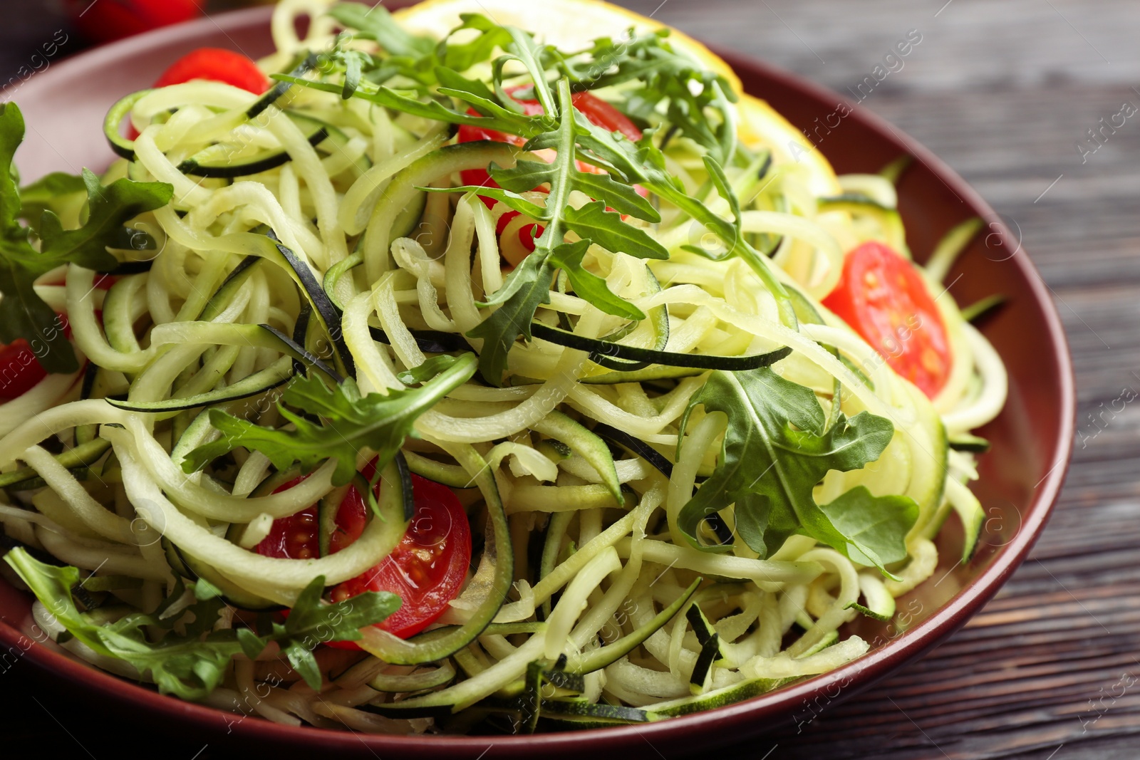 Photo of Delicious zucchini pasta with cherry tomatoes and arugula on black wooden table, closeup