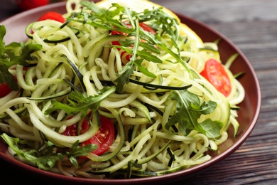 Photo of Delicious zucchini pasta with cherry tomatoes and arugula on black wooden table, closeup