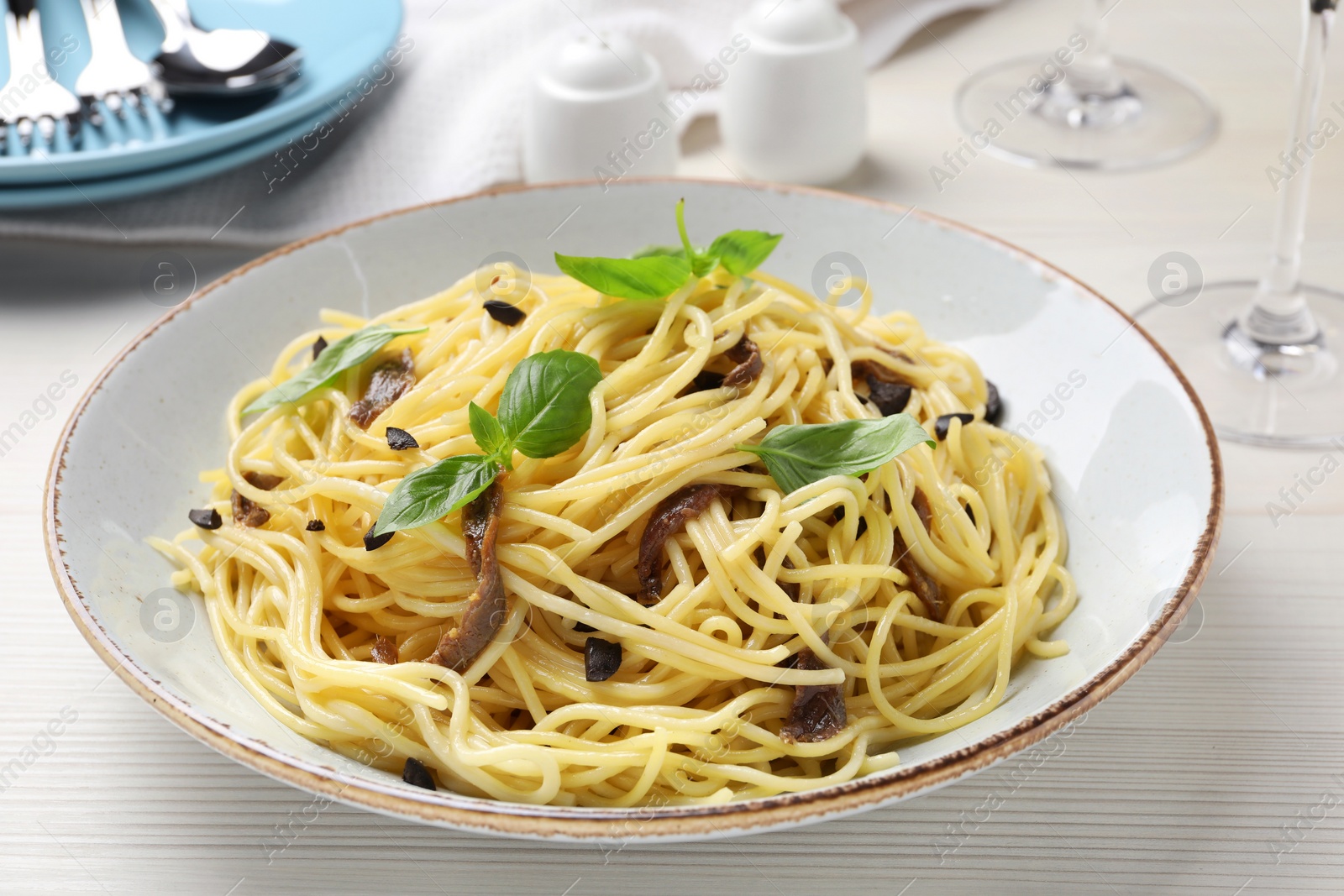 Photo of Delicious pasta with anchovies, olives and basil on white wooden table