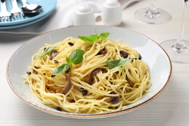 Photo of Delicious pasta with anchovies, olives and basil on white wooden table