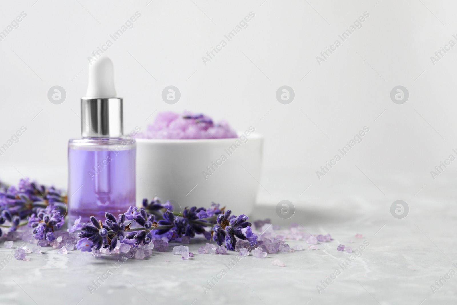 Photo of Natural cosmetic oil, bath salt, scrub and lavender flowers on grey marble table, space for text