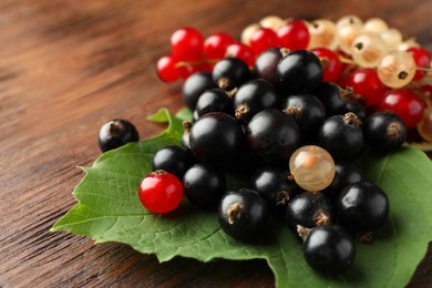 Different fresh ripe currants and green leaf on wooden table, closeup