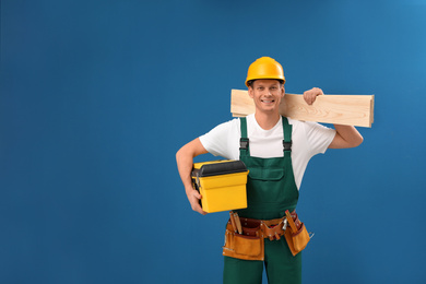 Handsome carpenter with wooden planks and tool box on blue background. Space for text