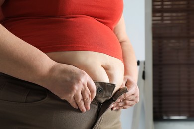 Photo of Overweight woman trying to button up tight trousers at home, closeup