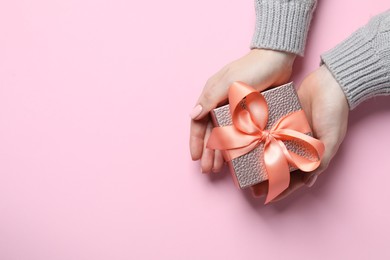 Photo of Christmas present. Woman holding gift box on pink background, top view. Space for text