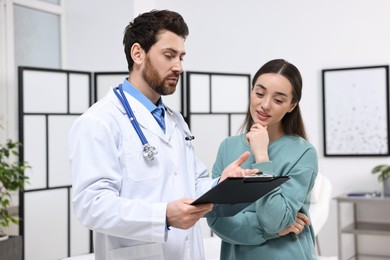 Photo of Doctor with clipboard consulting patient during appointment in clinic