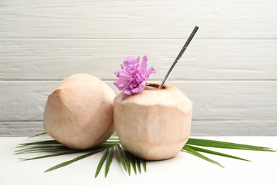 Photo of Young peeled coconuts with straw, palm leaf and flower on white wooden table