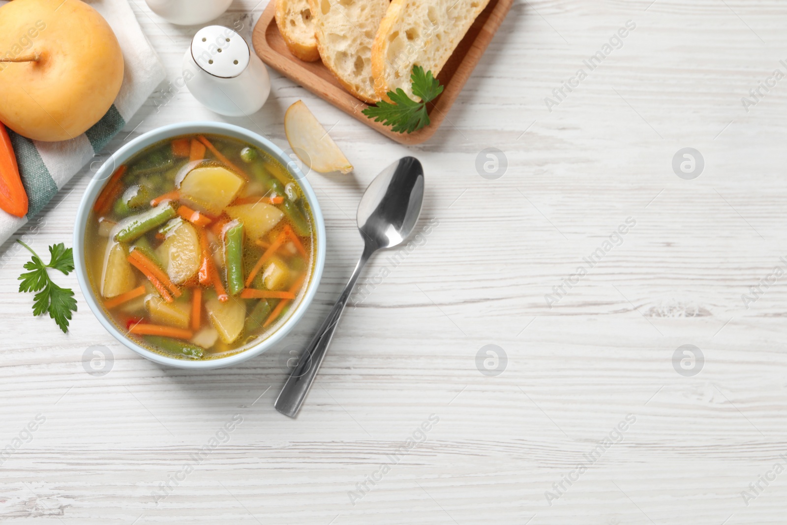 Photo of Bowl of tasty turnip soup with bread and spoon on white wooden table, flat lay. Space for text