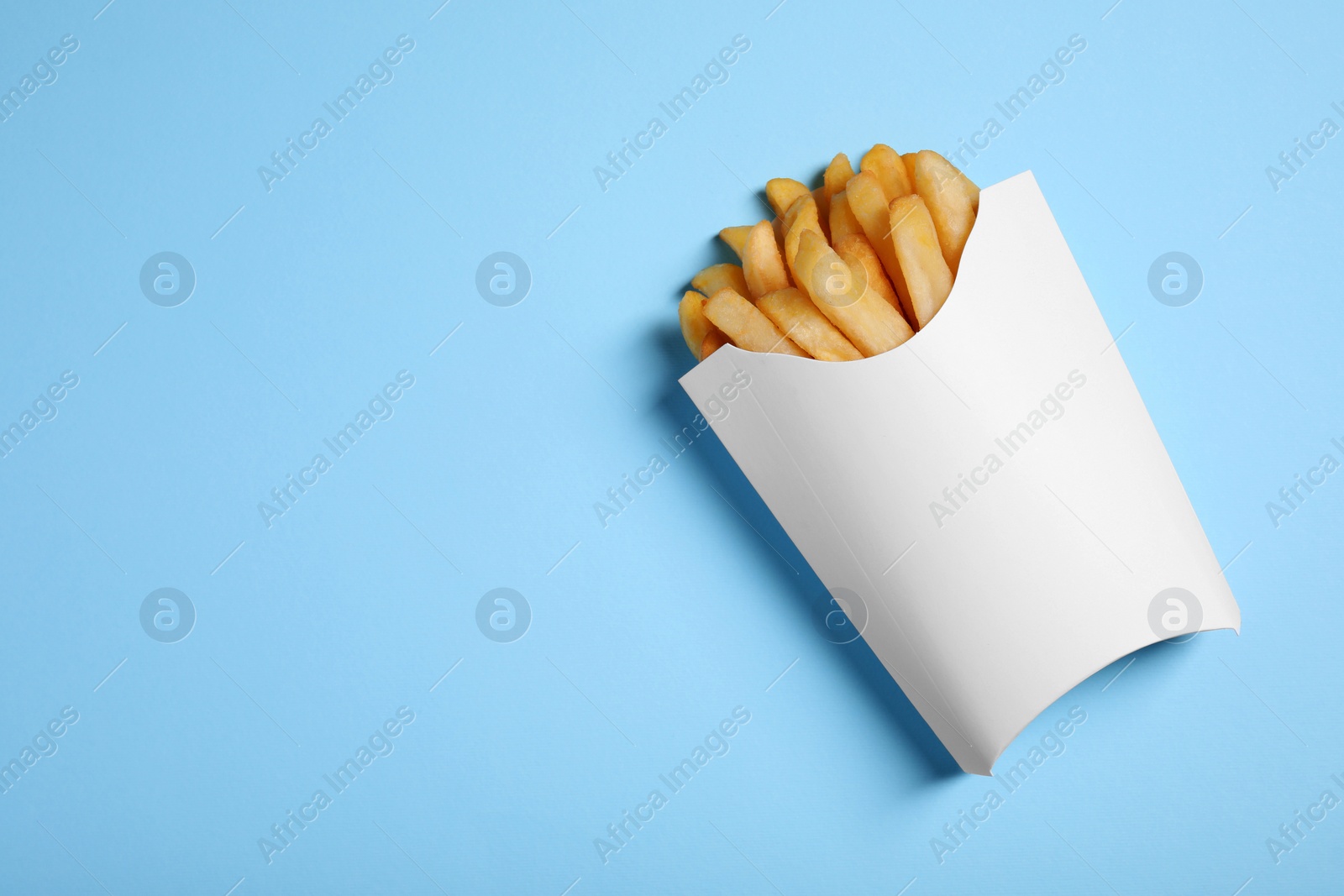 Photo of Paper cup with French fries on light blue table, top view. Space for text