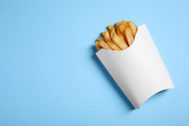 Photo of Paper cup with French fries on light blue table, top view. Space for text