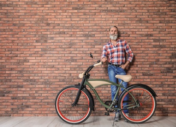 Portrait of handsome mature man with bicycle near brick wall