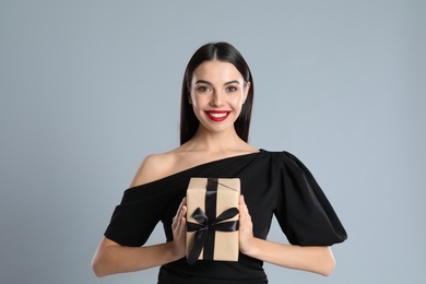 Photo of Woman in black dress holding Christmas gift on grey background