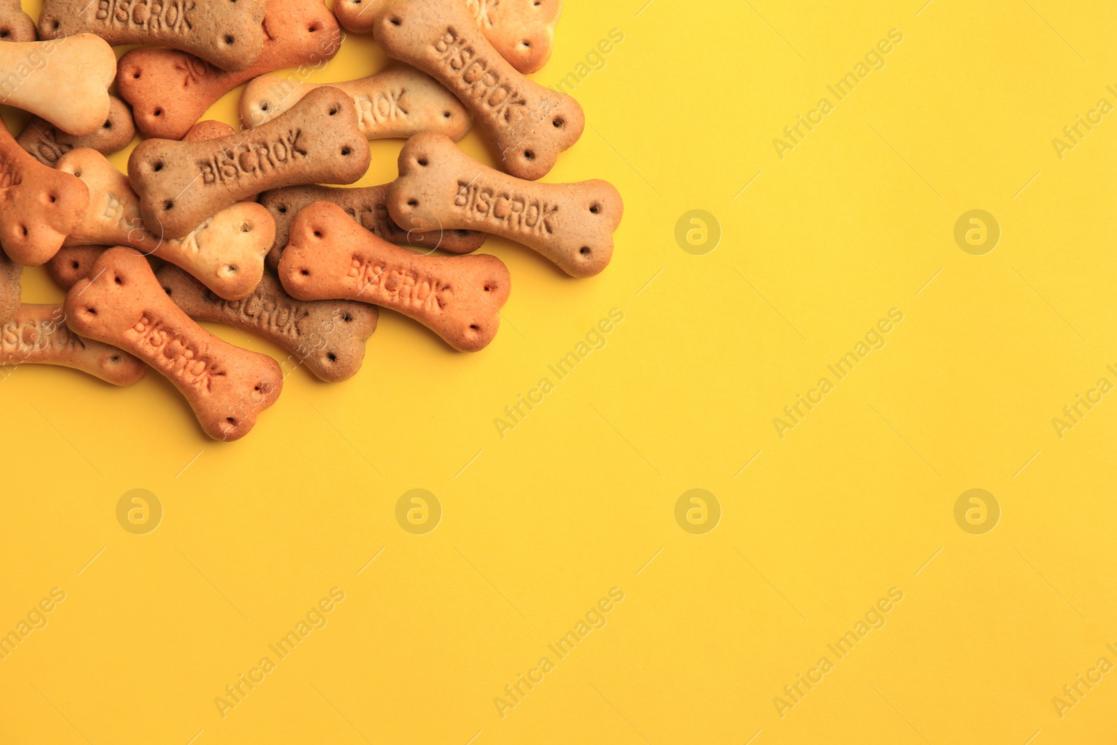 Photo of Bone shaped dog cookies on yellow background, flat lay. Space for text