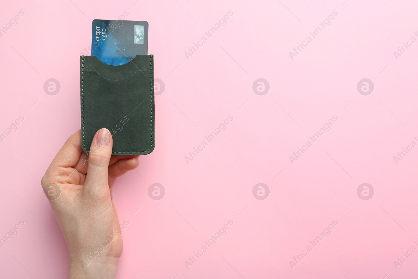 Photo of Woman holding leather card holder with credit card on pink background, top view. Space for text