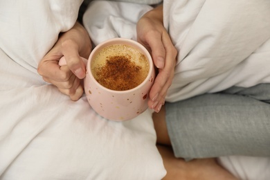 Woman with cup of coffee and soft blanket on bed, closeup