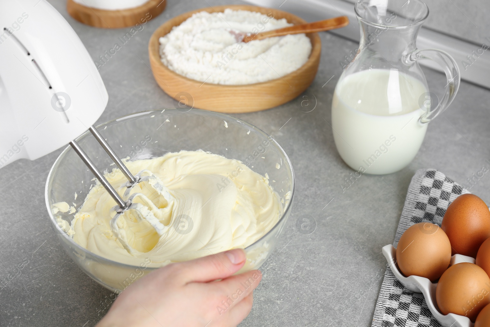 Photo of Woman whipping white cream with mixer at light grey table, closeup