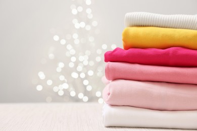 Photo of Stack of folded clothes on wooden table against beige background with blurred lights, space for text