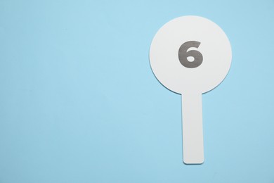 Photo of Auction paddle with number 6 on light blue background, top view. Space for text