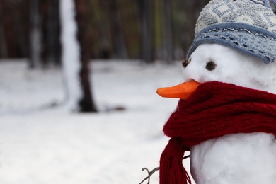 Funny snowman with scarf and hat in winter forest, closeup. Space for text