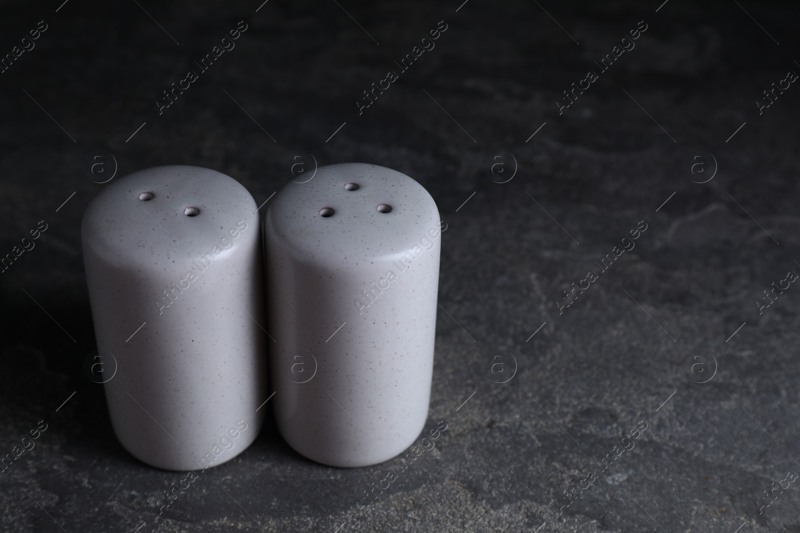 Photo of Salt and pepper shakers on dark textured table. Space for text