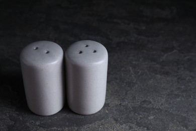 Photo of Salt and pepper shakers on dark textured table. Space for text