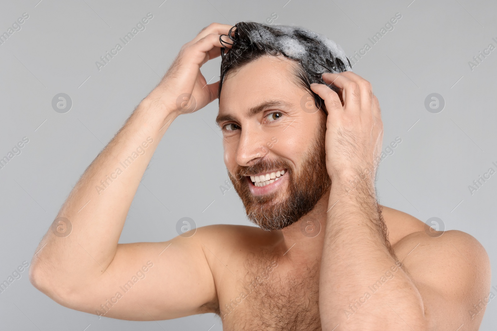 Photo of Happy man washing his hair with shampoo on grey background