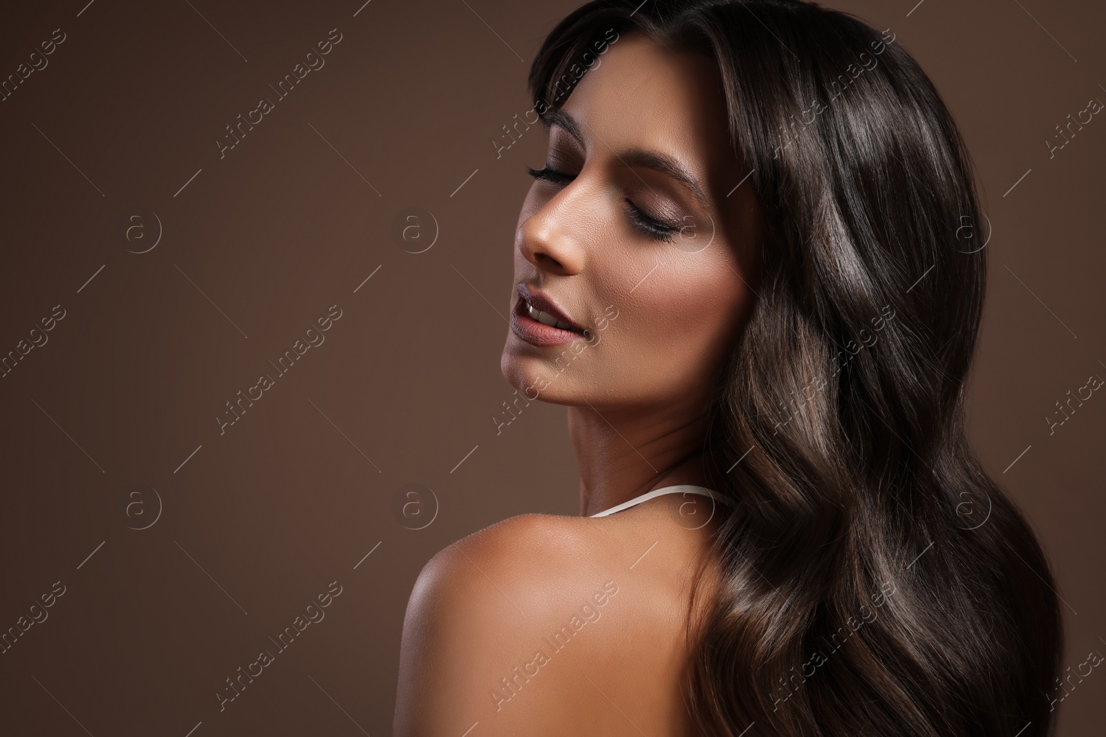 Image of Gorgeous woman with shiny wavy hair on brown background, space for text. Professional hairstyling