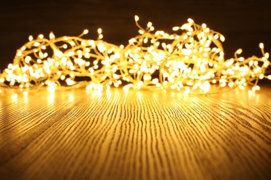 Photo of Beautiful glowing Christmas lights on wooden table. Space for text