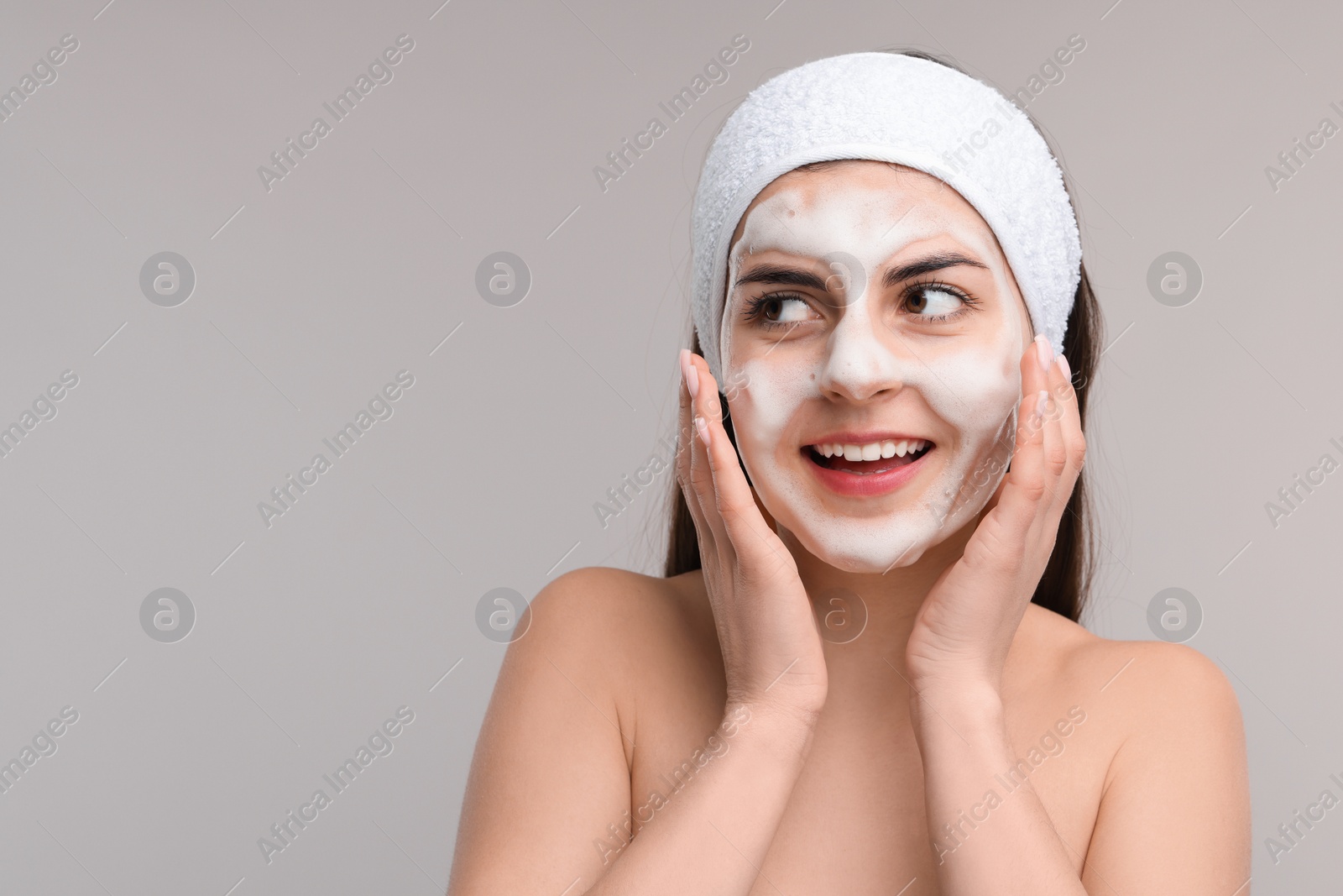 Photo of Young woman with headband washing her face on light grey background, space for text