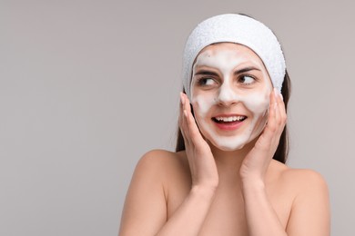 Young woman with headband washing her face on light grey background, space for text