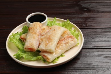 Photo of Delicious fried spring rolls with soy sauce on wooden table