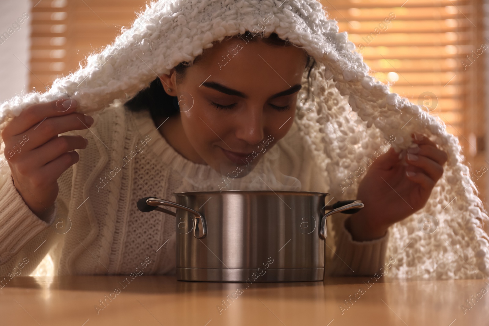 Photo of Woman with plaid doing inhalation above saucepot at table indoors