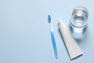 Plastic toothbrush with paste and glass of water on light background, above view. Space for text