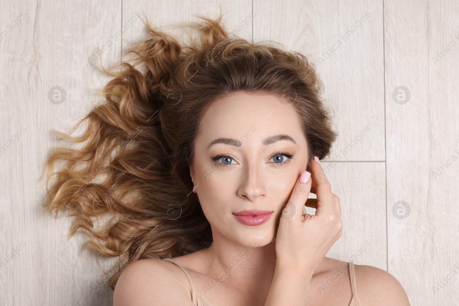 Photo of Portrait of beautiful woman with curly hair on wooden floor, top view