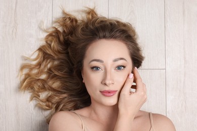 Portrait of beautiful woman with curly hair on wooden floor, top view