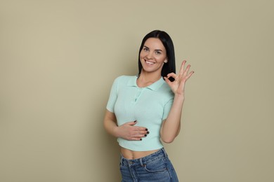 Happy woman touching her belly and showing okay gesture on beige background. Concept of healthy stomach