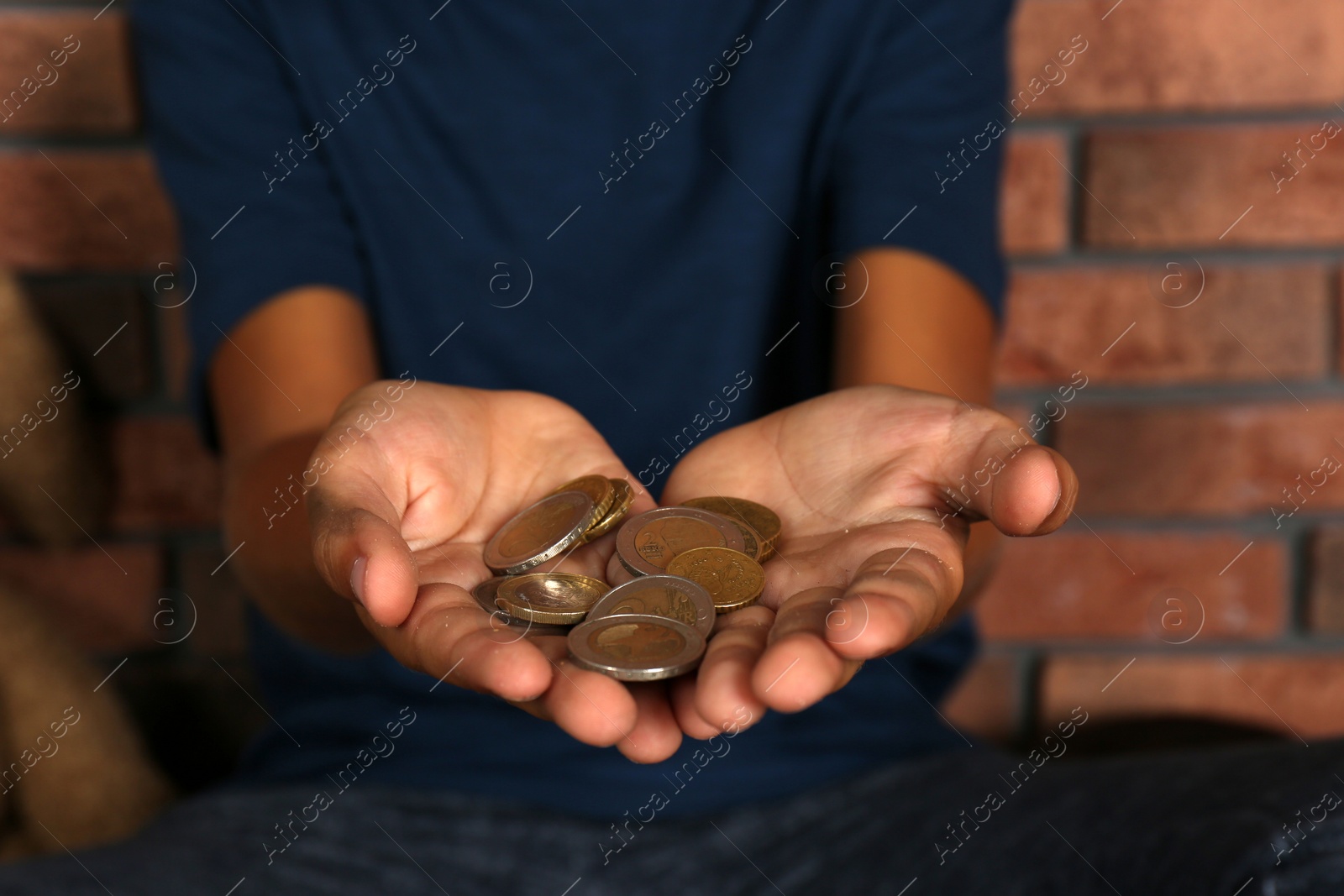 Photo of Poor homeless boy begging near brick wall, focus on hands