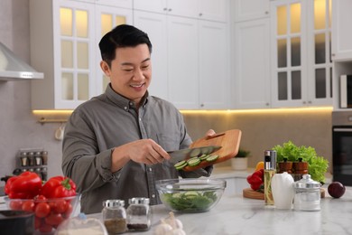 Cooking process. Man adding cut cucumber into bowl at countertop in kitchen