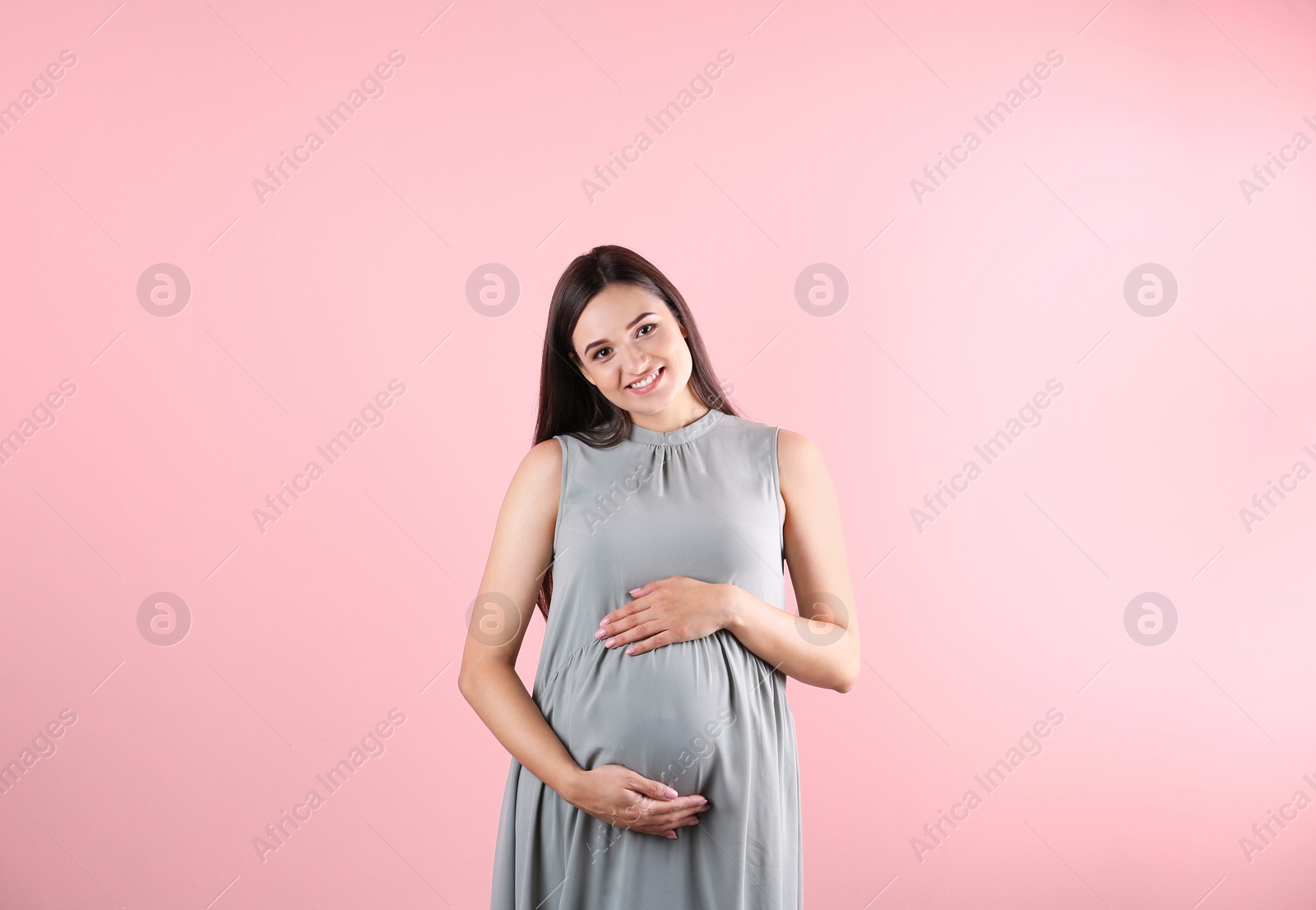 Photo of Beautiful pregnant woman holding hands on belly against color background