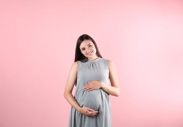 Beautiful pregnant woman holding hands on belly against color background