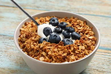 Photo of Bowl of yogurt with granola and blueberries on old wooden table, closeup