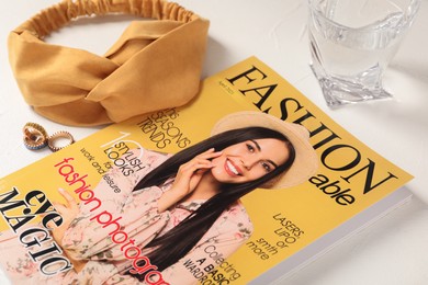 Photo of Fashion magazine, accessories and glass of water on white table
