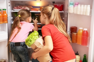 Young mother and daughter with paper bag full of food near refrigerator at home